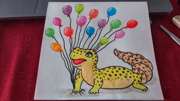 A finished card of a watercolour gecko holding balloons
